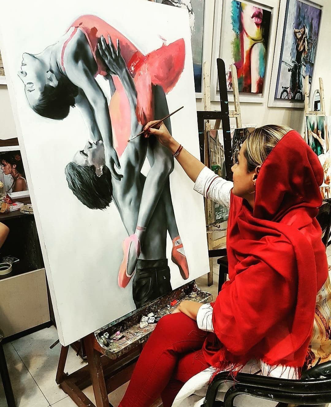 A student painting a striking red figure study on canvas